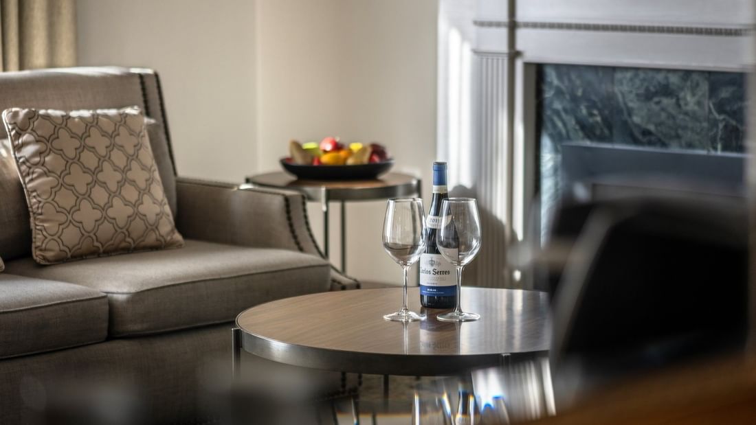Wine and glasses on a wooden table by a grey armchair near a fireplace in Balcony Junior Suite at Warwick San Francisco