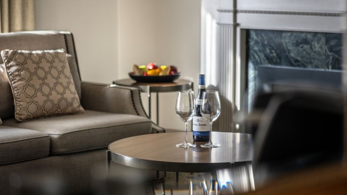 Wine and glasses on a wooden table by a grey armchair near a fireplace in Balcony Junior Suite at Warwick San Francisco