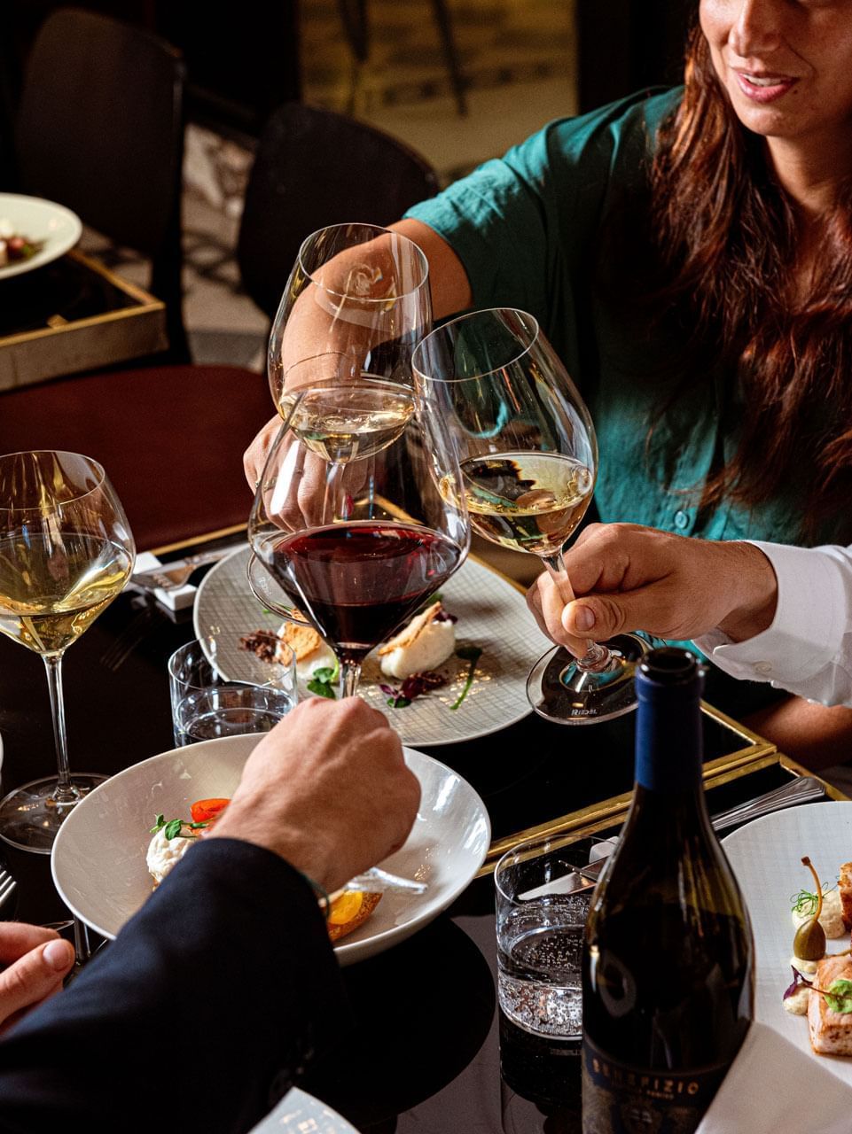 Two wine glasses toasting over a fine dining table set with elegant plates and a bottle of wine at AG Hotels