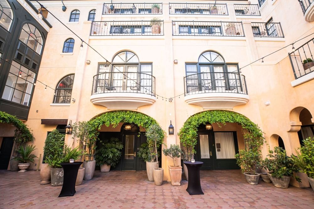 Outdoor courtyard featuring seating, event tables, and string lights, surrounded by lush greenery at El Prado Hotel