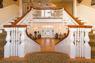 A grand central staircase with white banisters and wooden handrails in the main lobby of The Stanley Hotel