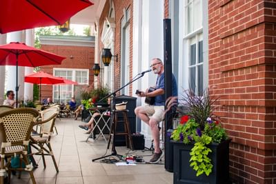 Musician playing a guitar by a brick wall under patio umbrellas surrounding a terrace at Rodd Charlottetown Hotel