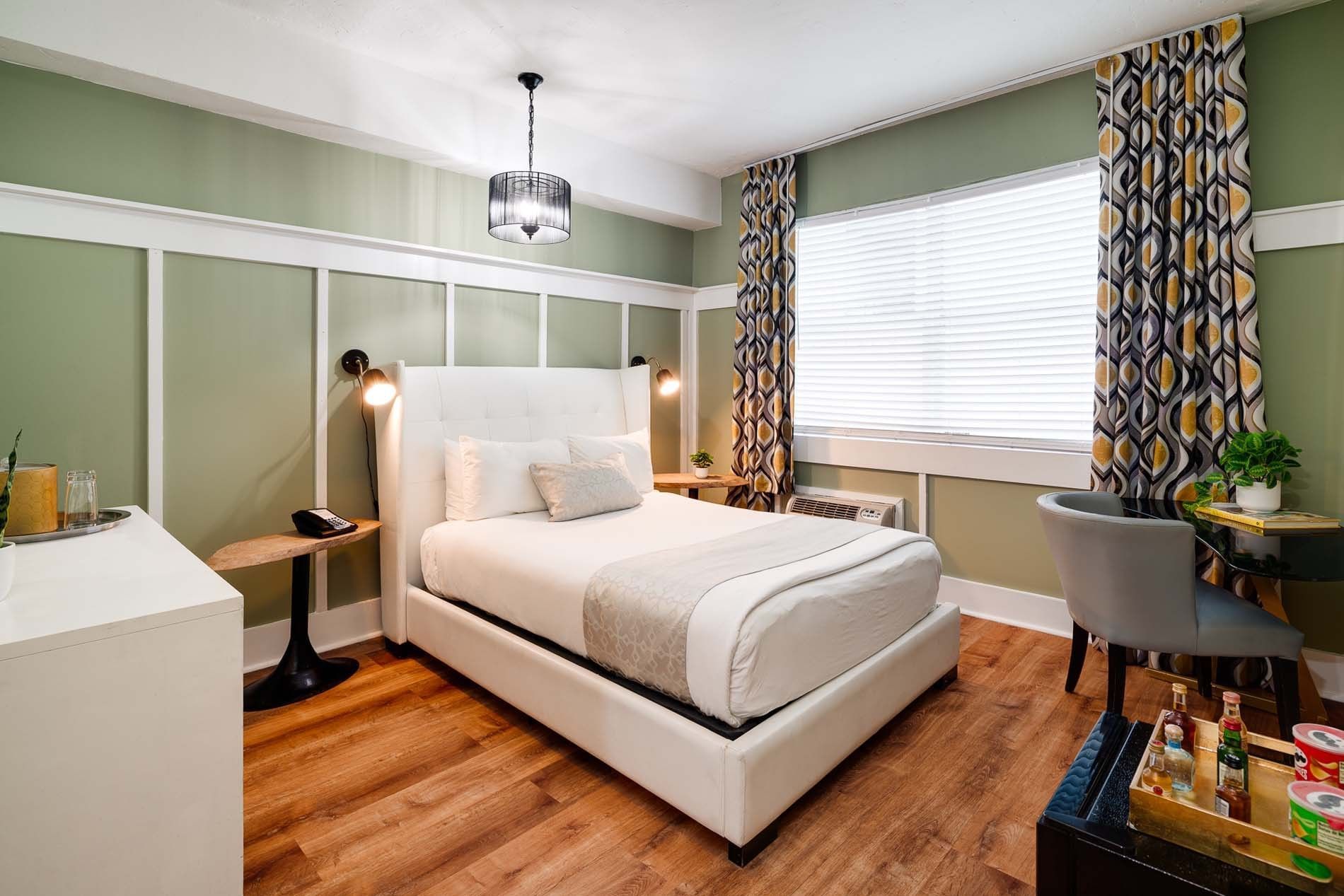 A hotel room with a white bed, green walls, and wood floors.