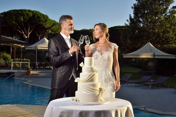 Wedded couple toasting champagne by the outdoor pool at Golf Hotel Punta Ala