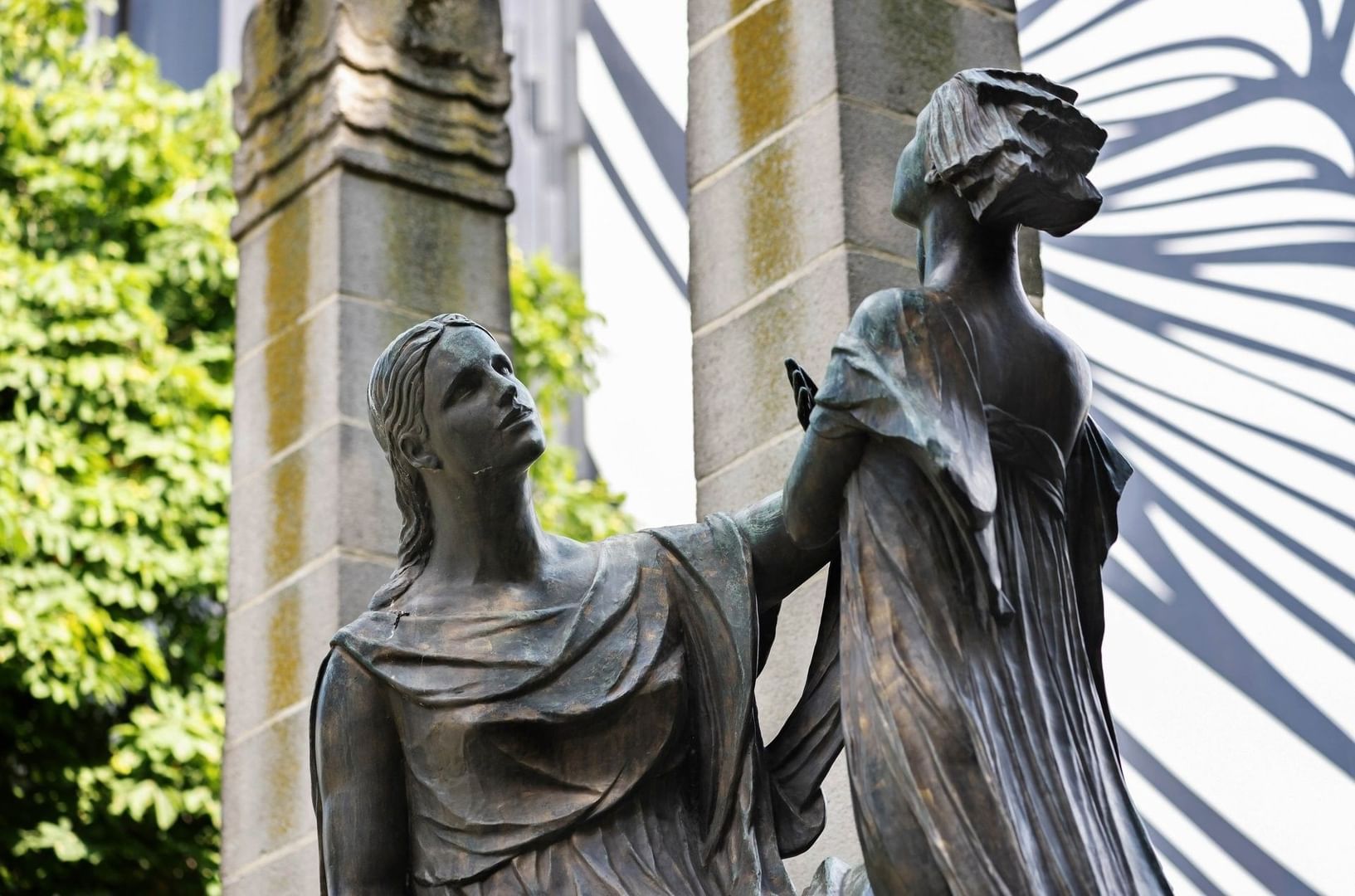 Two stone statues of women standing against a stone wall 