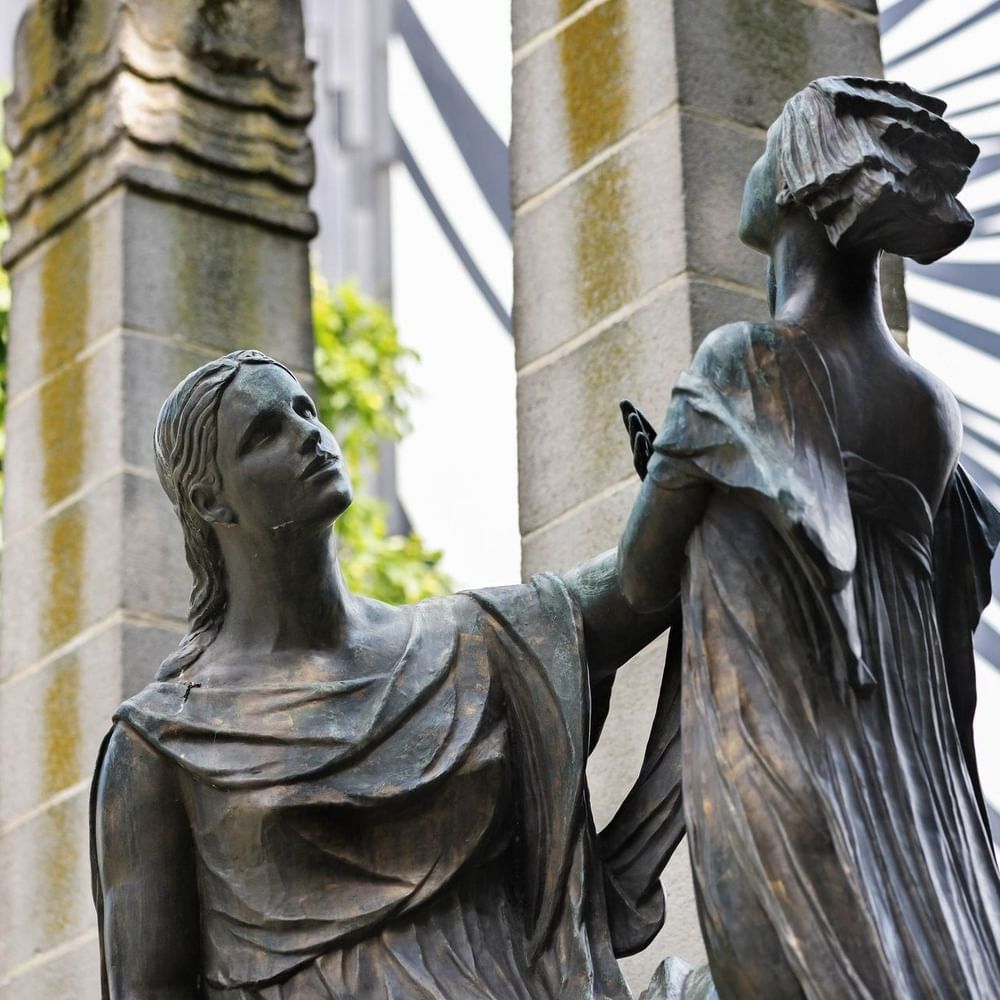 Bronze statue of two women in draped clothing beside stone pillars at Hotel Barsey by Warwick