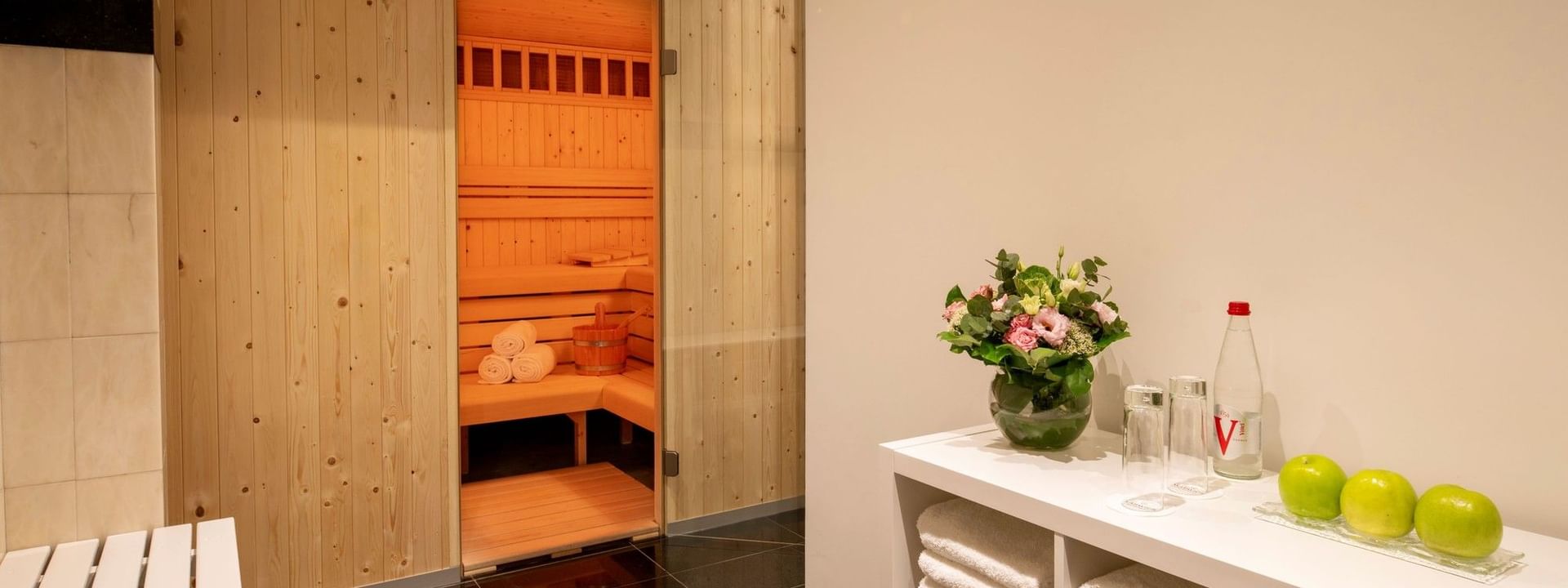 Sauna en bois avec bancs et étagère blanche avec serviettes et pommes vertes au Warwick Brussels Grand-Place