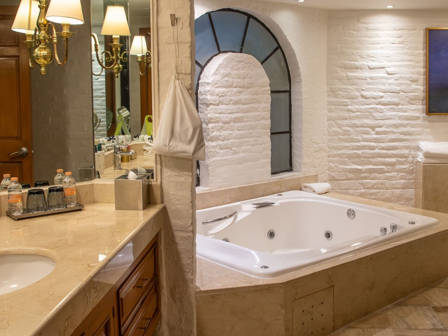Baño elegante con jacuzzi, paredes de piedra blanca y arco decorativo en Suite Presidencial King en Quinta Real Guadalajara
