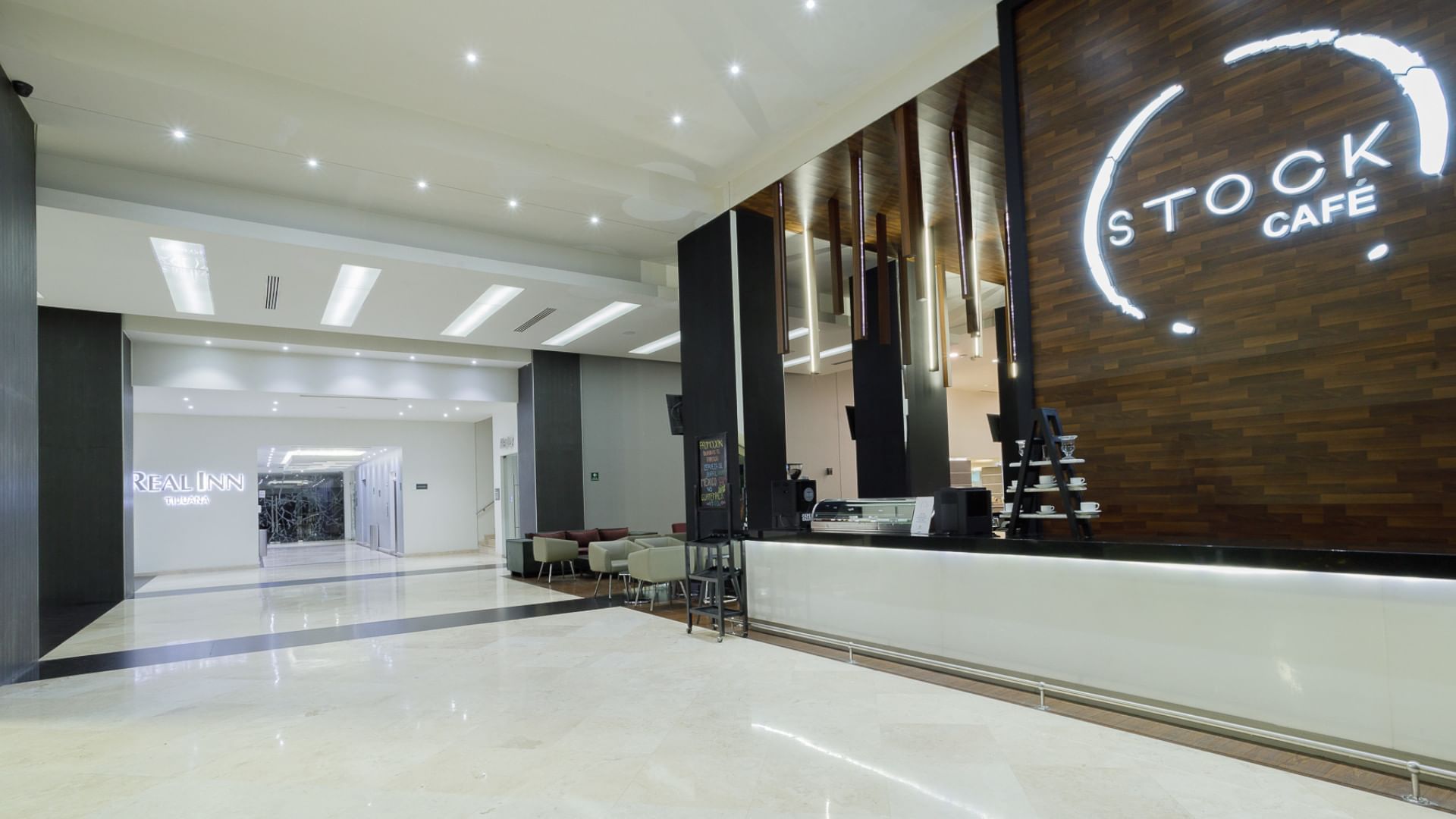 The Stock Café entrance with wood paneling and a modern glowing logo, located at the Real Inn Tijuana