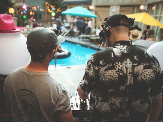 Two DJs with headphones operate a soundboard at an outdoor pool party at Paradox Summit Lodge.