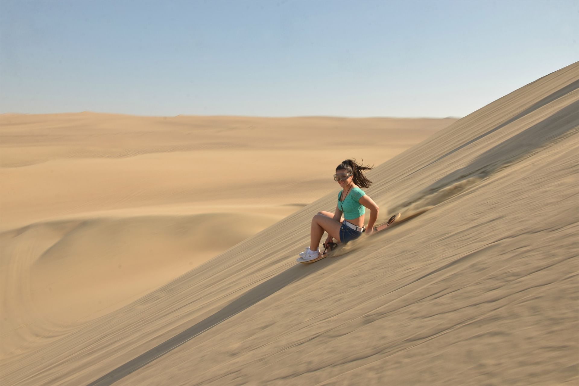 A lady sits on a sunny steep dune, featuring Desert Adventures Peru near Las Dunas Resort Ica