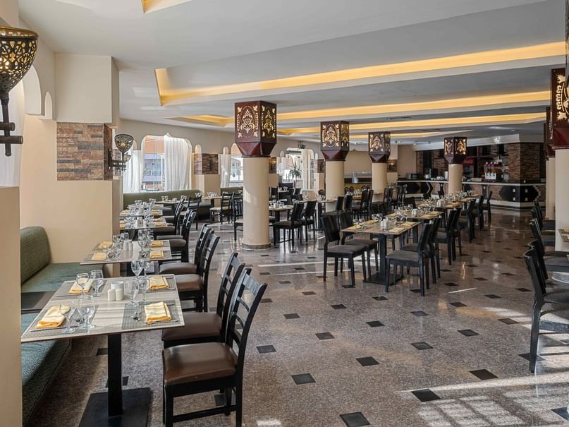 Elegantly decorated restaurant with set tables, cushioned benches, and patterned floor under a high ceiling with warm lighting.