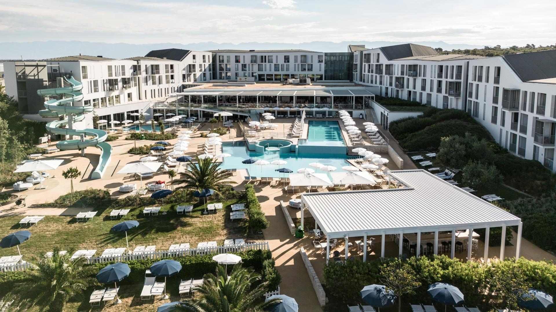 Zračna slika luksuznog hotelskog kompleksa s bazenima, suncobranima i kliznim stazama.