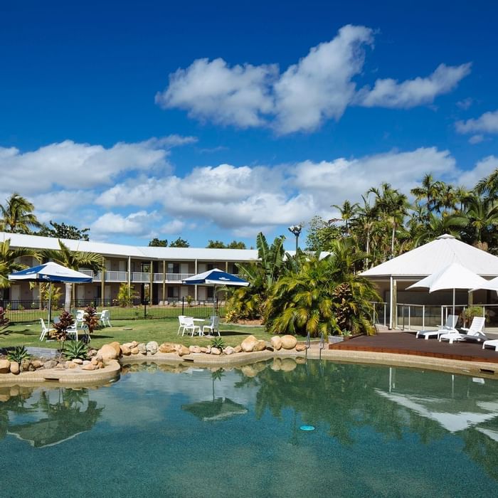 Serene pool area with lounge chairs & umbrellas surrounded by tropical plants at Mercure Hotel Townsville