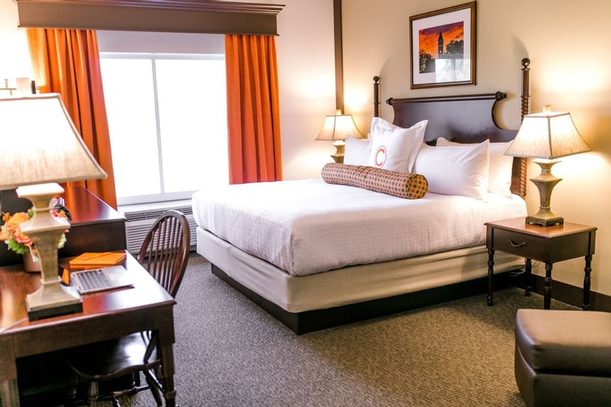 King bed beside a desk and orange window drapes in Executive King Lakeside at Clemson University Conference Center & Inn