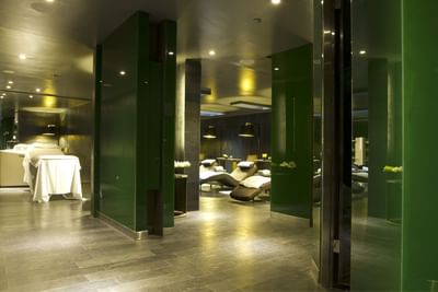 Salón de spa con sillas de masaje, iluminación suave y paredes verdes reflectantes.