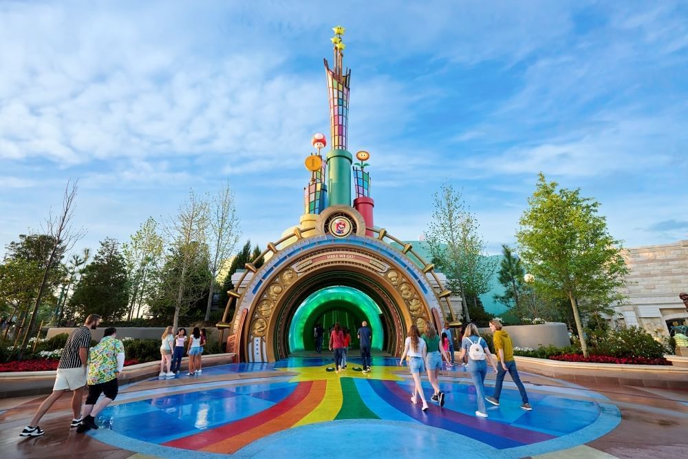 A rainbow pathway leads into a colorful portal with various mushrooms and flowers emerging from pipes.