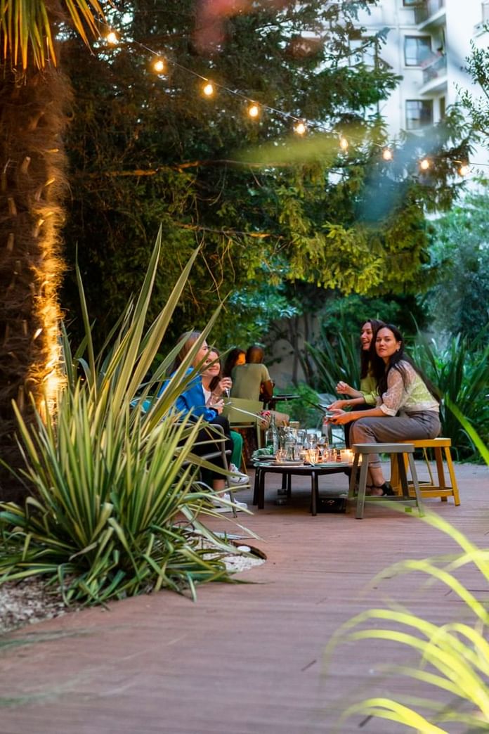 Friends gathered by a table with glassware & culinary surround by trees at Oceania Hotels