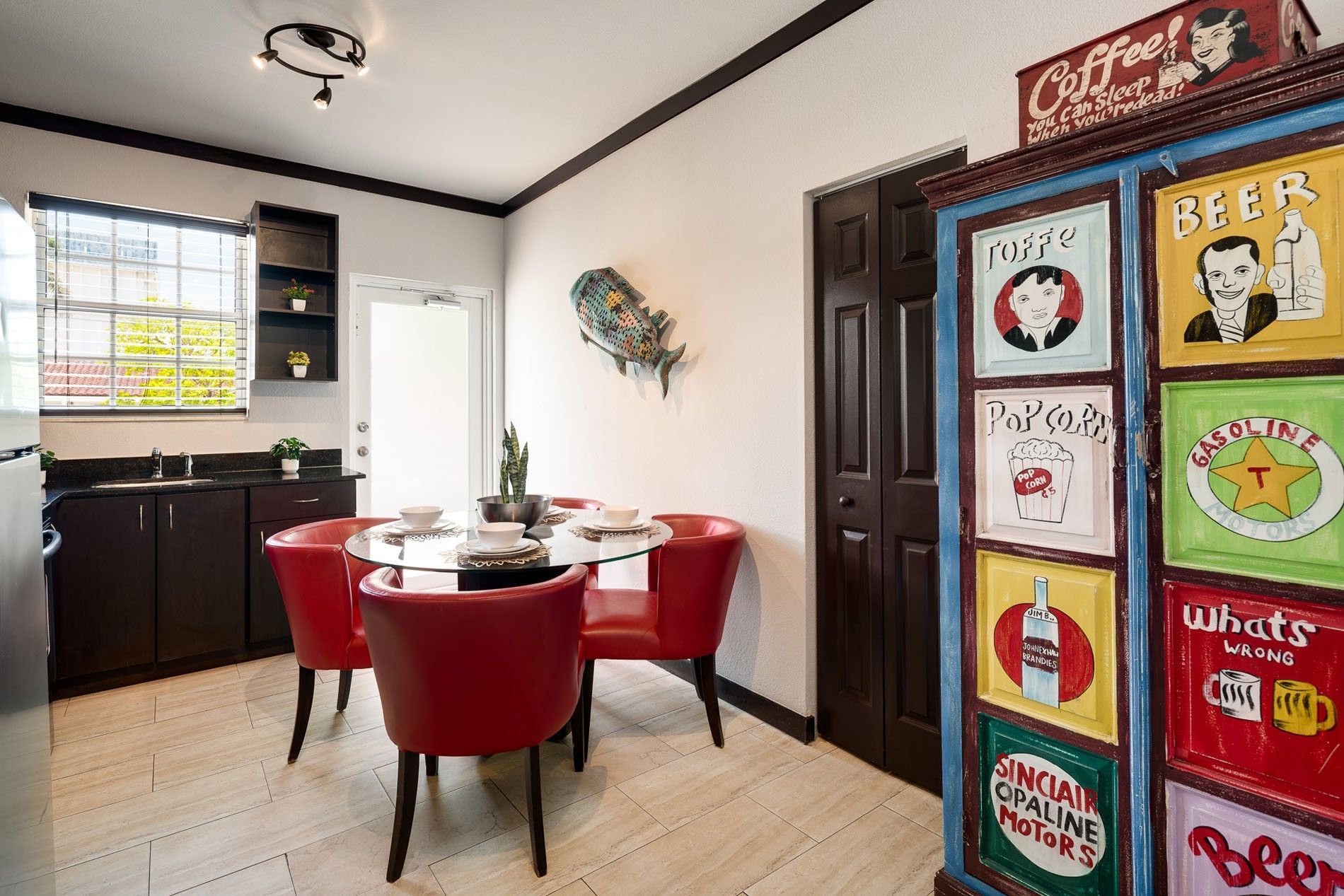 A dining area with a glass table, red chairs, and retro signs on a cabinet.