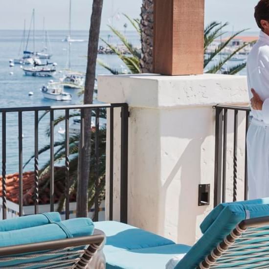 A couple in robes by a balcony railing overlooking a marina with yachts at Catalina Island Company, one of the things to do on Catalina Island