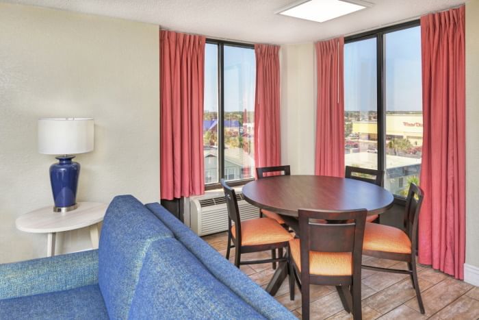 A hotel room with a dining table, sofa, and window