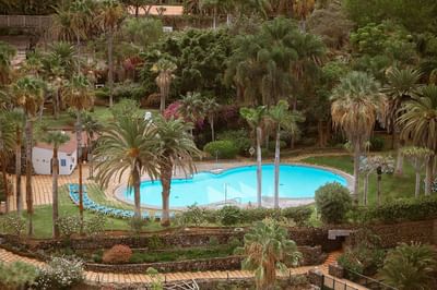 Aerial view of a resort with a large pool surrounded by palm trees and lounge chairs.
