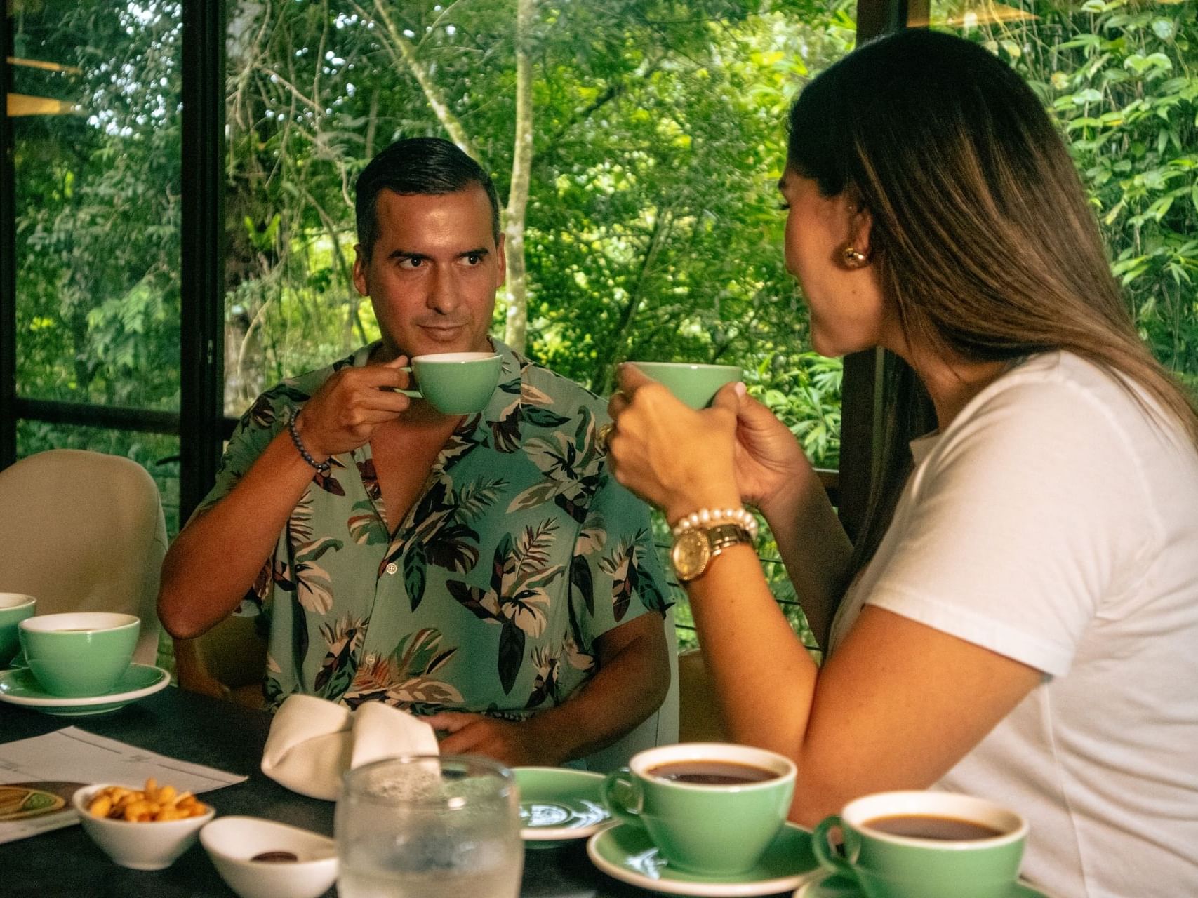 Two people sipping coffee in a table with a green outdoor backdrop at El Silencio Lodge and Spa