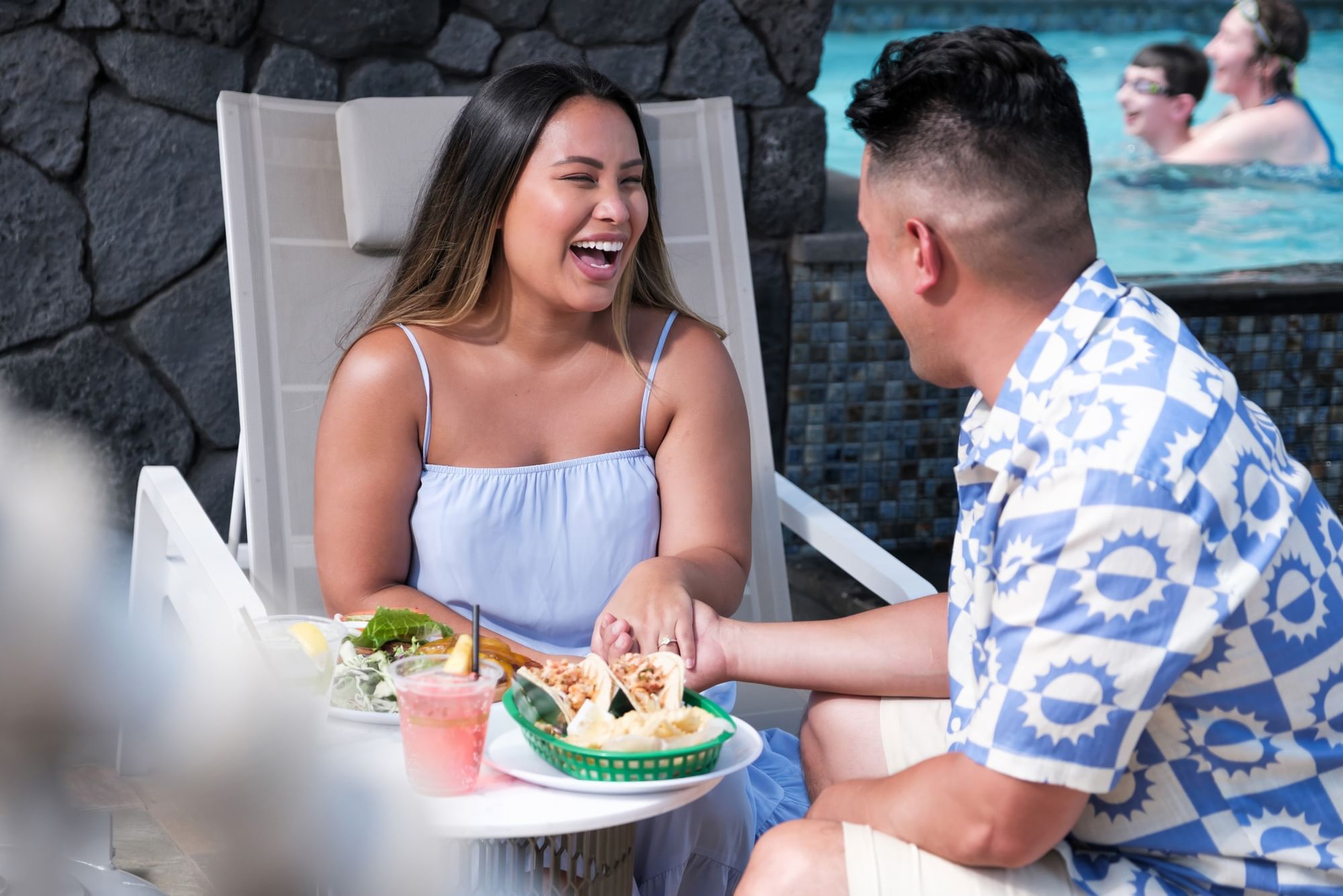 A couple enjoys a meal and drinks by the pool.