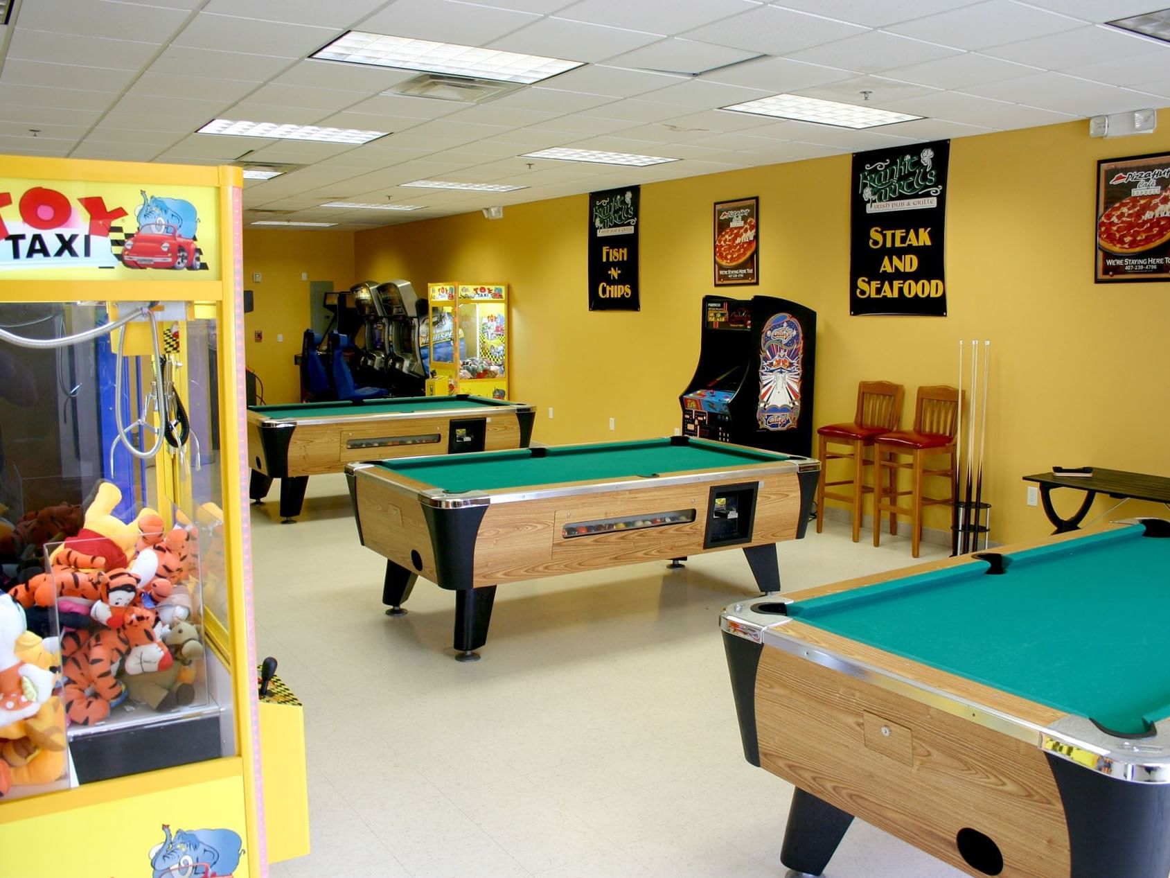 a game room with pool tables, arcade games, and a stuffed animal dispenser