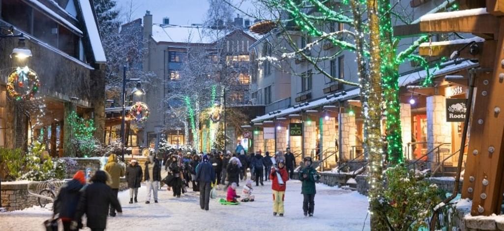 Visitors walking through snow-covered Whistler Village, surrounded by festive holiday lights and shops.