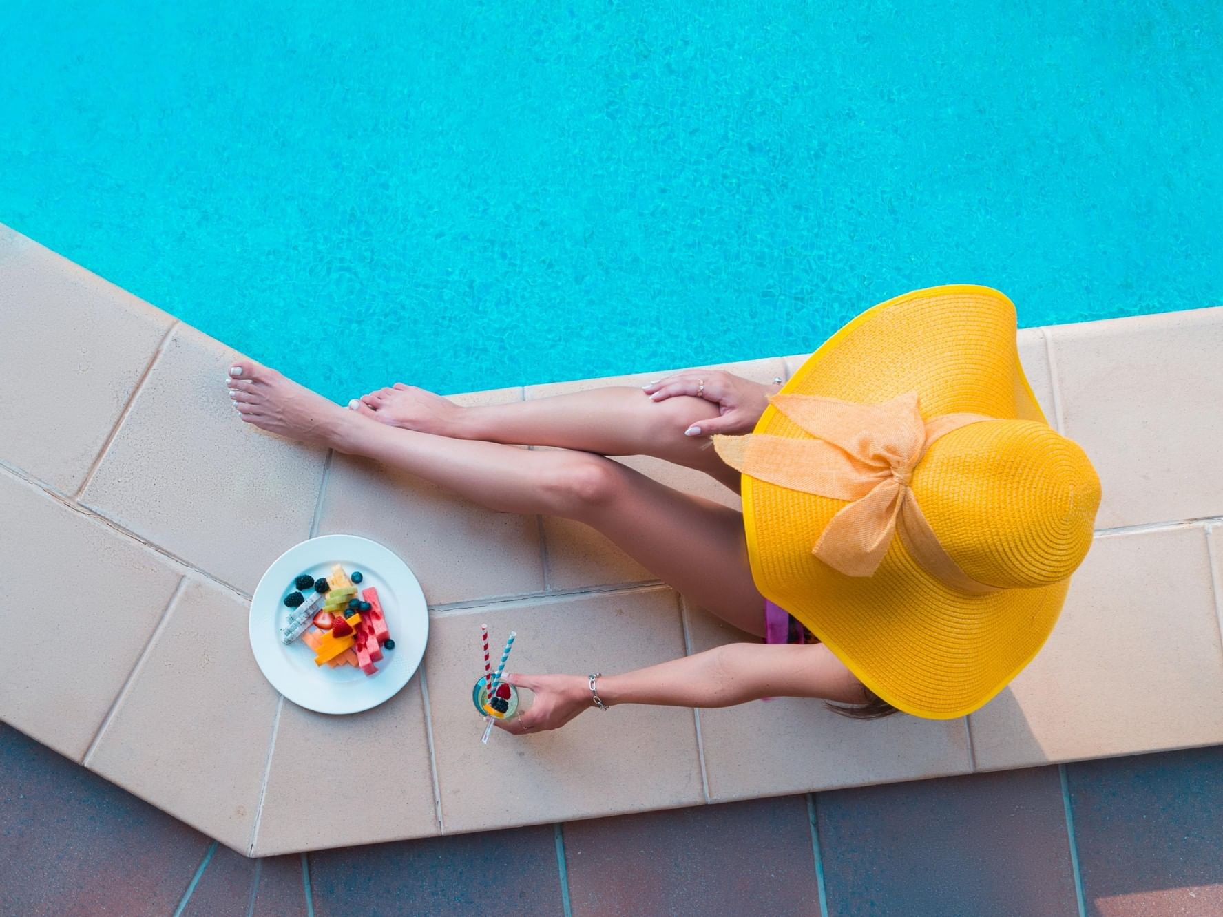 Guest relaxing poolside at Hotel Grand Chancellor Townsville rooftop pool with fresh fruit and a tropical drink.