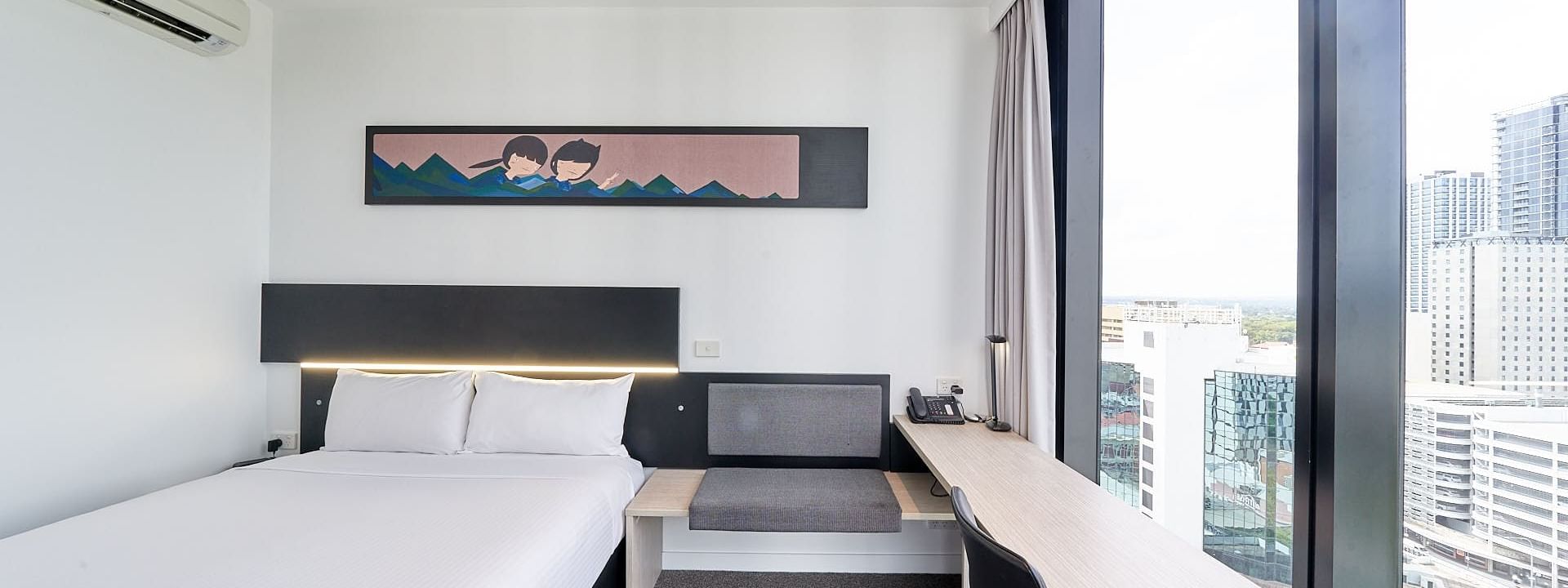 Cozy bed with hanging wall art and seating by the window in Superior Room, One Queen Bed City View at Ibis Adelaide