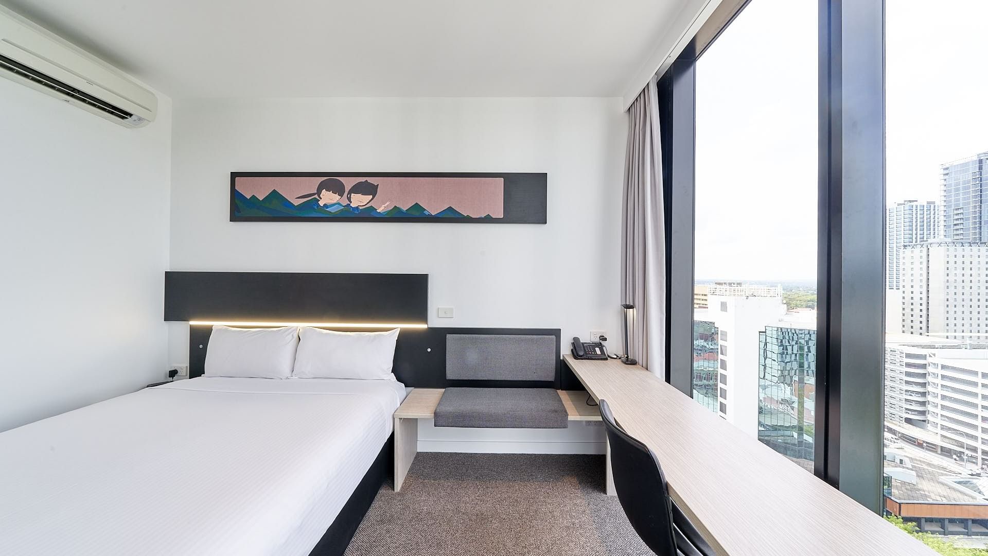 Cozy bed with hanging wall art and seating by the window in Superior Room, One Queen Bed City View at Ibis Adelaide