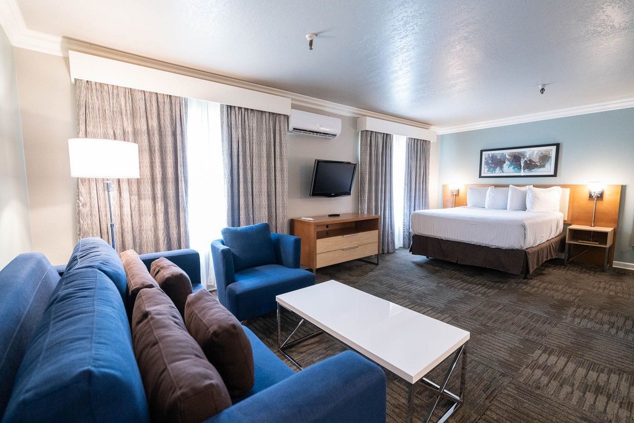 A hotel room with a blue sofa, chair, coffee table, and bed