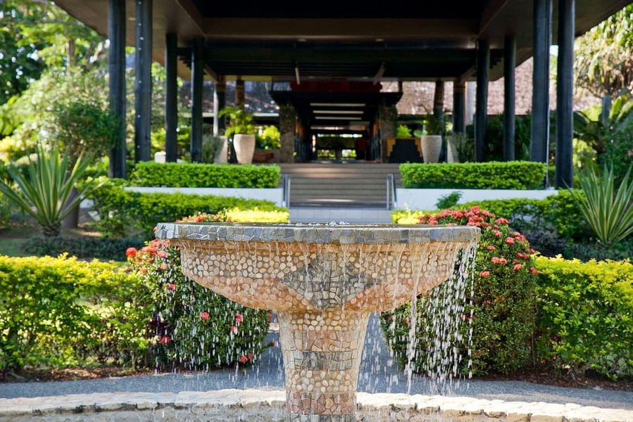 Stone water fountain by green hedges under a dark pavilion roof at The Naviti Resort - Fiji