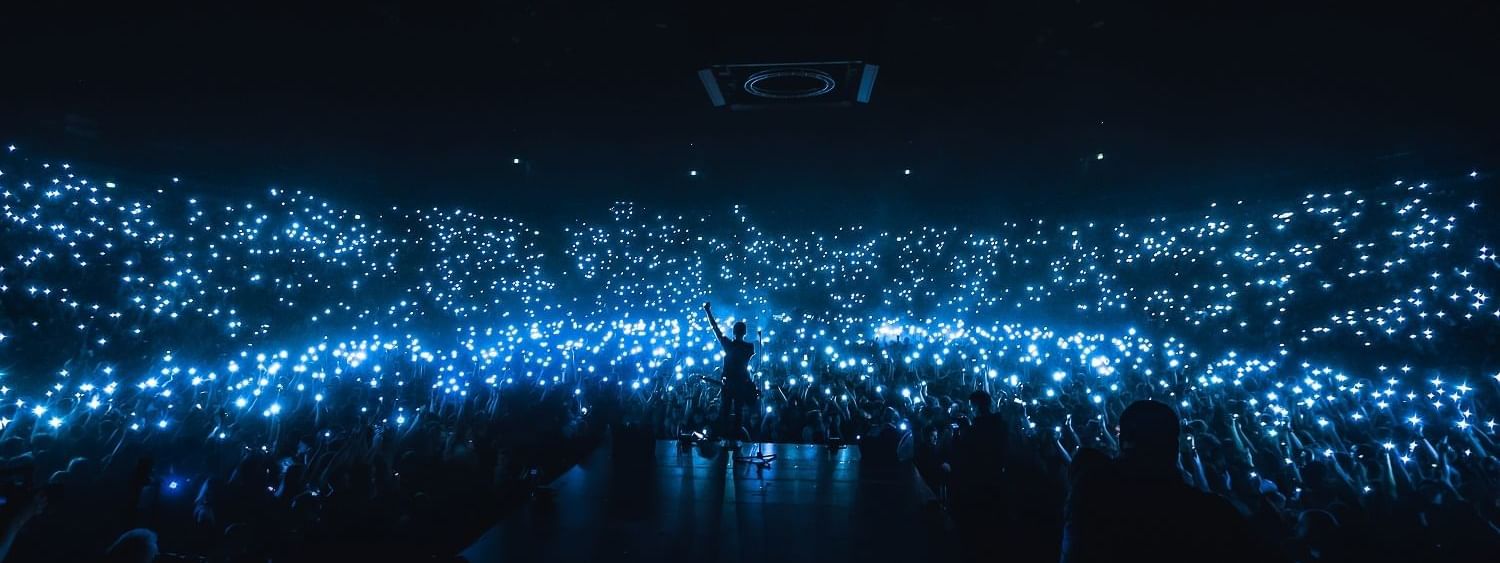 Performer on stage, surrounded by a sea of fans waving illuminated phones at Accor Stadium near Novotel Sydney Olympic Park
