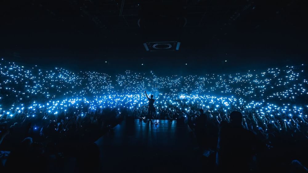 Performer on stage, surrounded by a sea of fans waving illuminated phones at Accor Stadium near Novotel Sydney Olympic Park