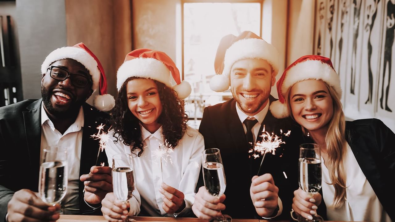 four people with Santa hats smiling with drinks and sparkles in hand