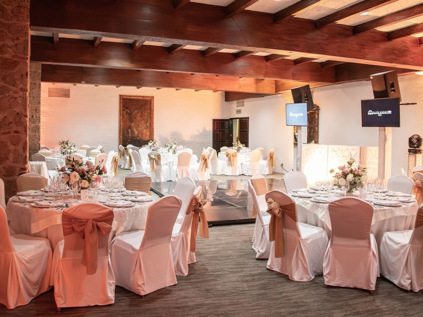 Salón Virreinal features elegant round tables with white linens and coral sashes under exposed wood beams at Quinta Real Guadalajara