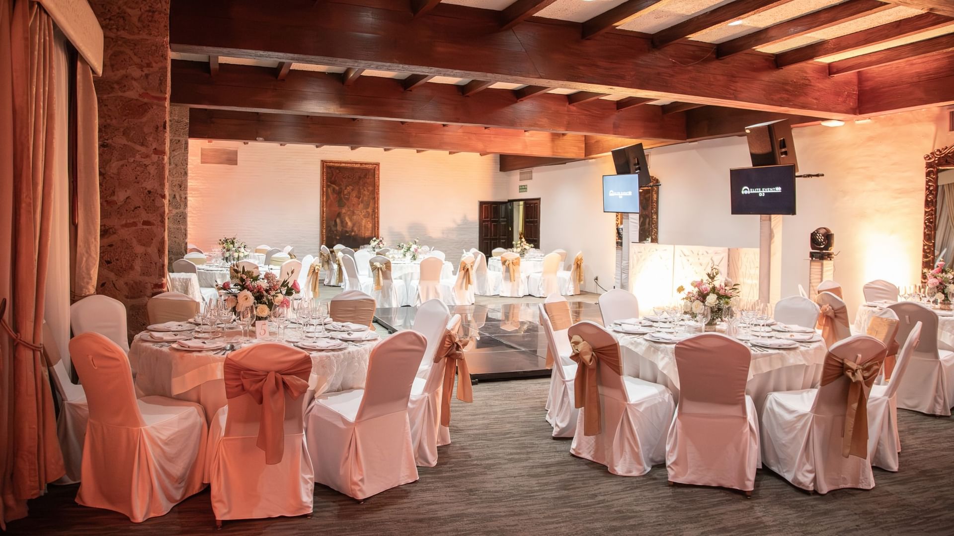 Salón de eventos con mesas redondas decoradas con manteles blancos y lazos coral en Quinta Real Guadalajara
