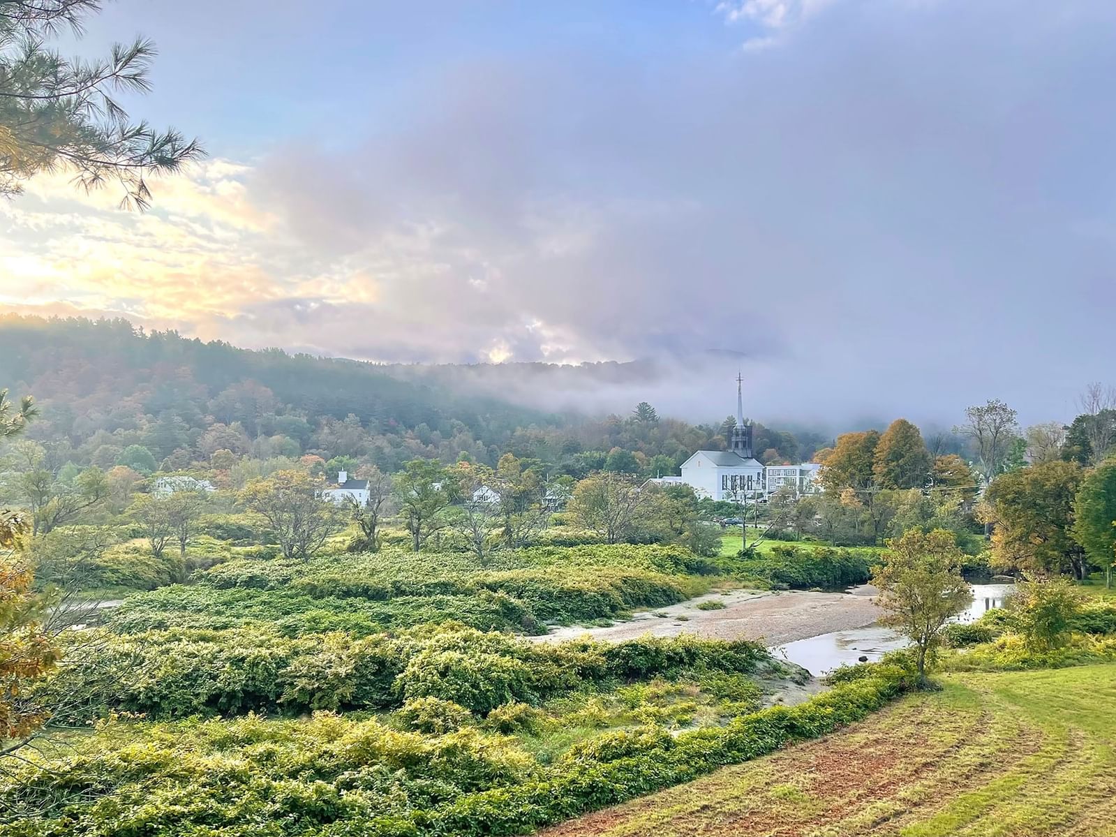 Foggy morning landscape with a river and buildings.