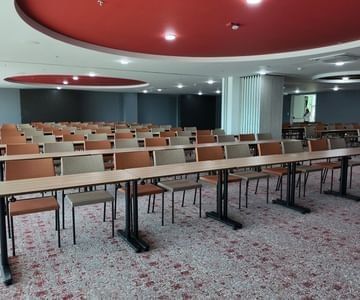 Salón Yerbabuena con mesas largas y filas de sillas bajo paneles circulares rojos en Unika Hotels, hotel de élite en Bogotá