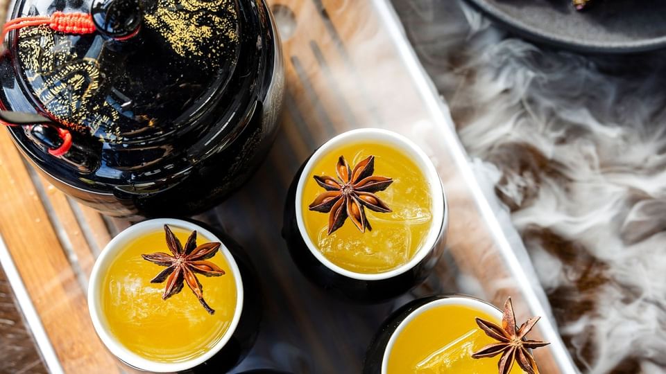 Théière noire avec trois tasses de boisson jaune garnie d'anis étoilé servie au restaurant de l'hôtel X