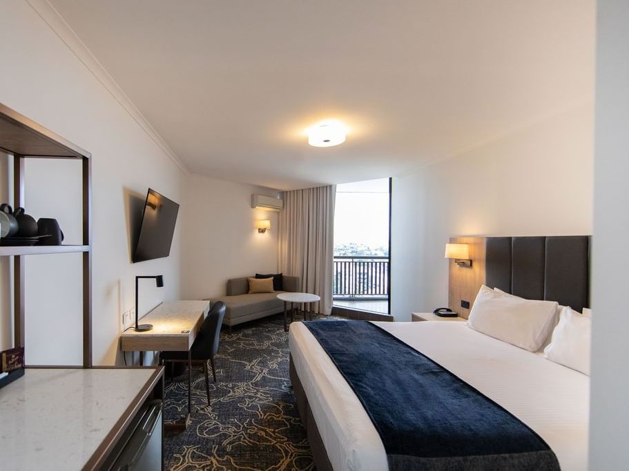 Bed with side lamp and work area in Deluxe King Balcony Room at Hotel Grand Chancellor Brisbane