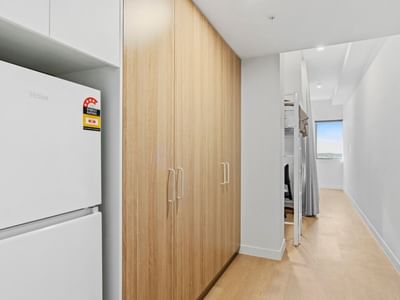 Hallway with white refrigerator, wooden closet, and bunk beds at UniLodge Brisbane City.