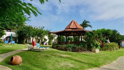 Lounge chairs on a green lawn beside a wooden gazebo with a red tiled roof at the Sugar Cane Club Hotel & Spa
