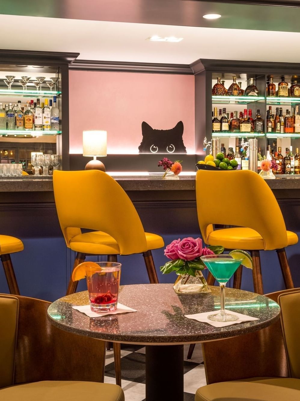 Yellow chairs by a round table with cocktails under a bar with a cat silhouette at Warwick Denver
