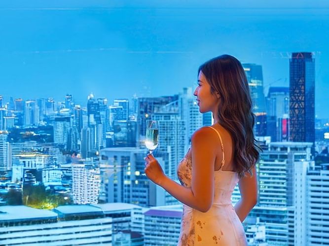  A woman in a flowing dress stands overlooking the city, immersed in the view and the atmosphere of urban life.