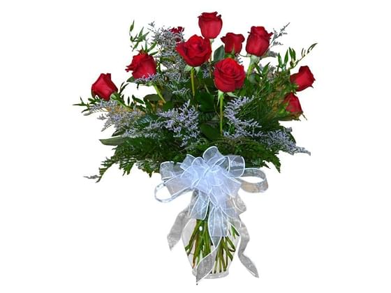 A dozen roses arranged in a vase with a white bow