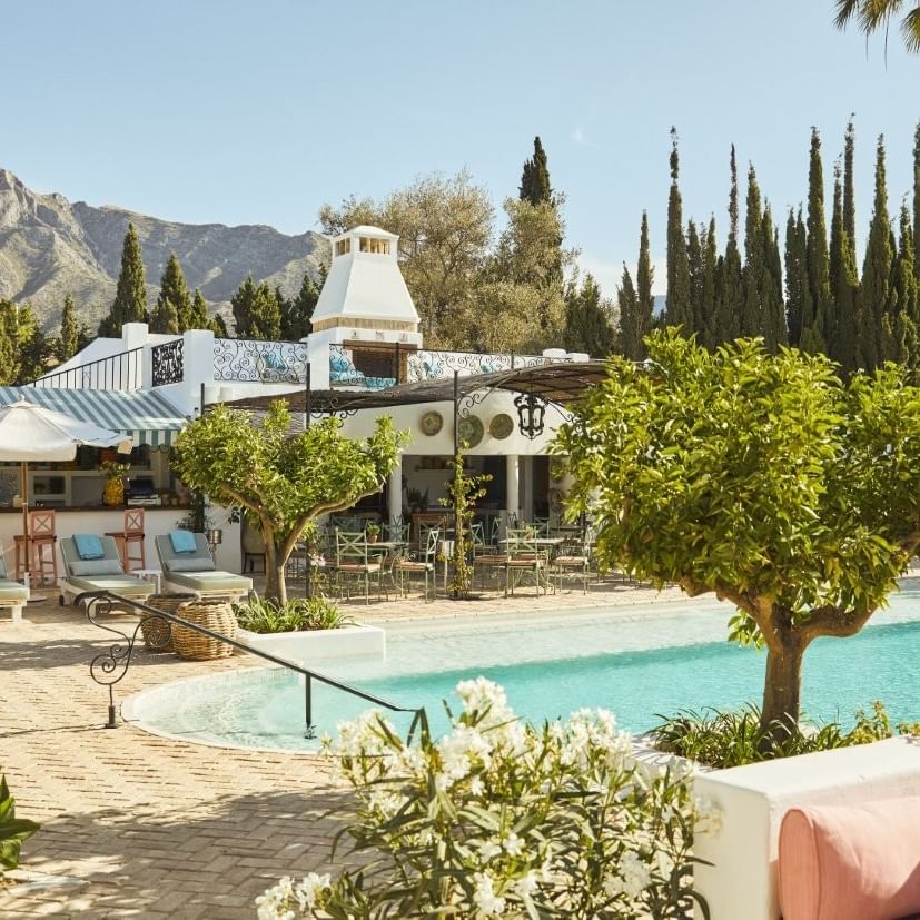 Piscina al aire libre y área de descanso rodeada de árboles y flores.